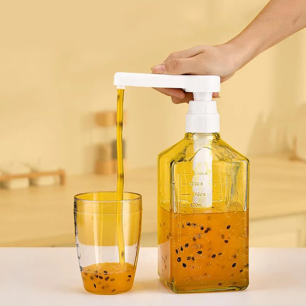 A hand is dispensing a yellow syrup from a precision pump dispenser into a glass container.