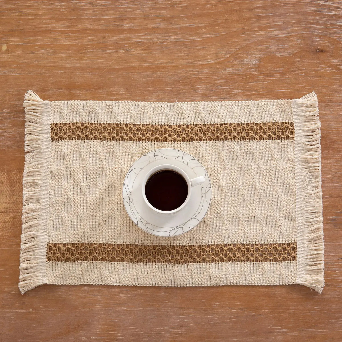 Keramische Tasse mit dunklem Kaffee auf einem gewebten Jute-Platzdeckchen mit Baumwollfransen.