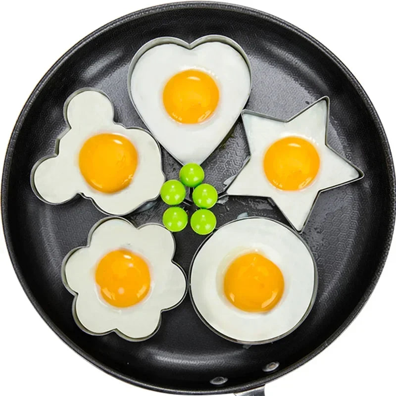 A black frying pan contains five perfectly cooked fried eggs in various shapes like hearts and stars.