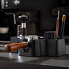 A black universal coffee tamper base with wooden handles and various espresso tools is shown on a dark surface.
