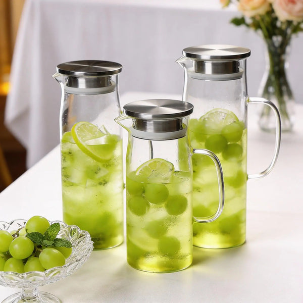 Drei Glaswassergefäße mit grünem Flüssigkeit und Limettenscheiben auf einem weißen Tisch.