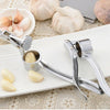 Stainless steel garlic press and mincer tool with several cloves of garlic on a white cutting board