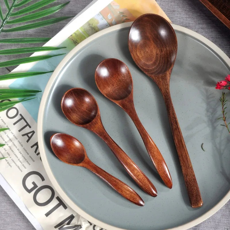 A set of four dark brown wooden stirring spoons arranged on a light gray plate next to a green leaf and paper.