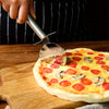 A hand is using a stainless steel pizza wheel cutter to slice a pizza on a wooden board.
