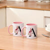 A white coffee mug with a pink handle and a large black monogram design featuring pink floral accents.
