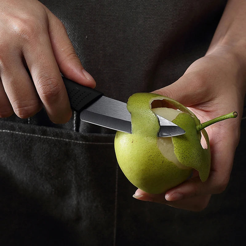 A hand holds a stainless steel utility knife slicing open a green apple.