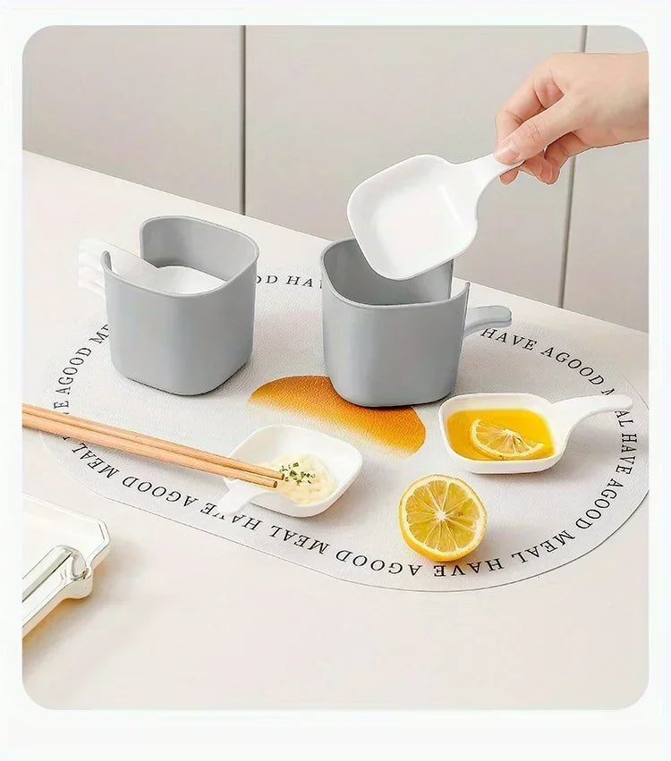 A hand is pouring oil from a white spoon into a gray plastic sauce dish set for seasoning and serving.