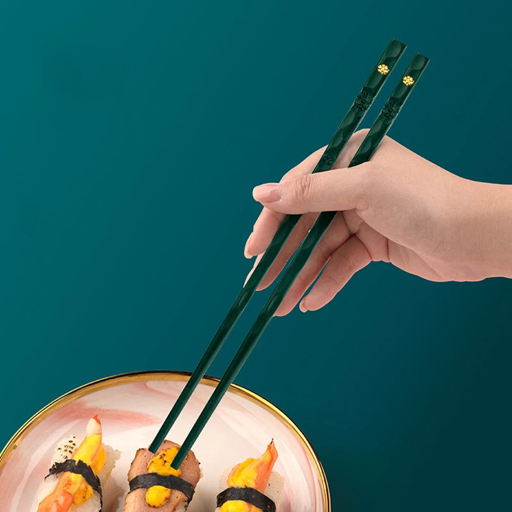 A hand holds a pair of dark green reusable Japanese and Korean chopsticks over a plate of food.
