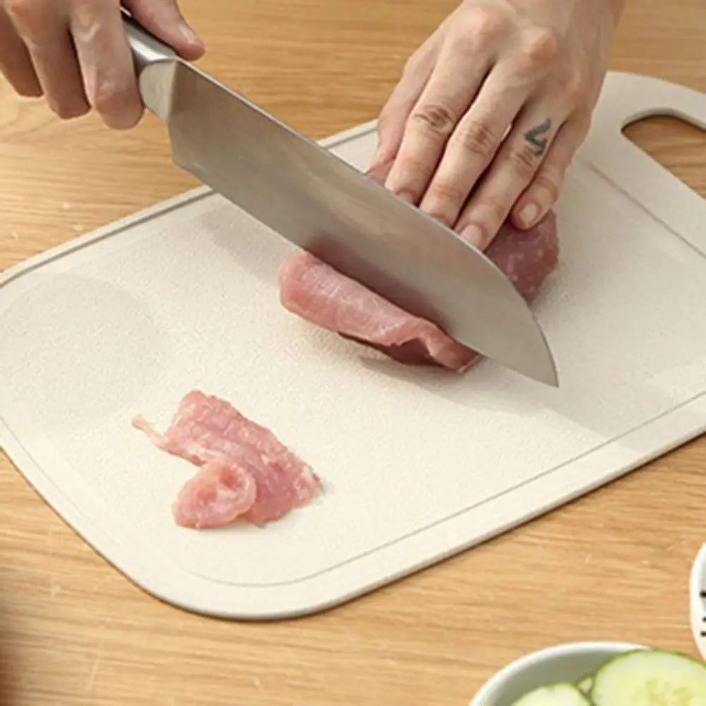 Hands are using a knife to cut pink meat on a light-colored non-slip plastic cutting board.