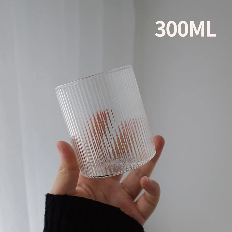 A hand holds a clear, ribbed glass tumbler with a reddish tint against a white background.