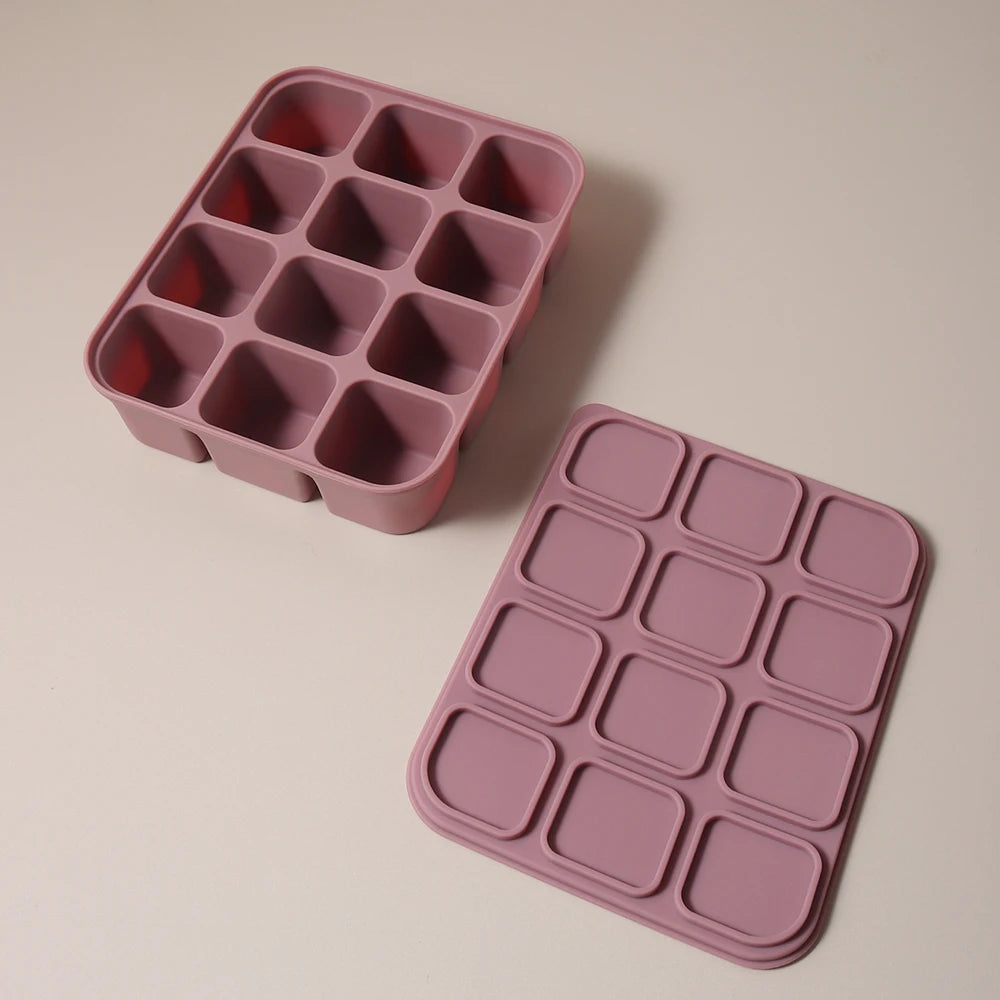 A pink silicone food tray with multiple compartments for baby purees is shown on a light surface.