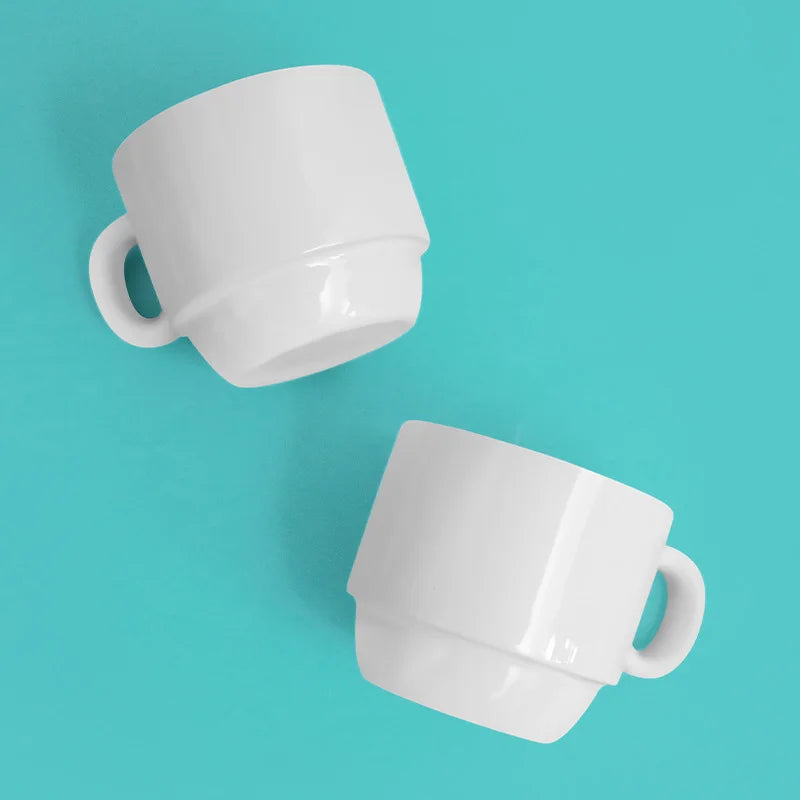 A white ceramic cappuccino cup with a handle is shown against a light blue background.