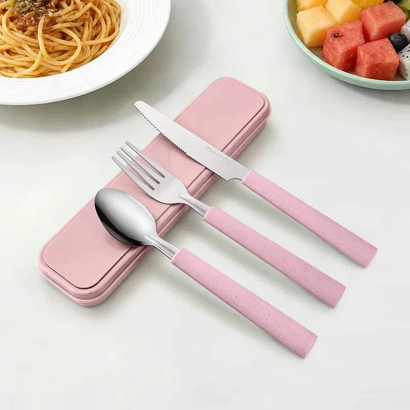 A pink portable stainless steel cutlery set with a matching storage case is displayed next to a bowl of fruit.