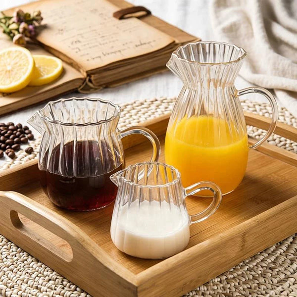 A wooden tray holds striped borosilicate glass pitchers containing orange juice and milk.