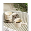 A set of white ceramic espresso coffee cups displayed on a glass tray with green foliage in the background.