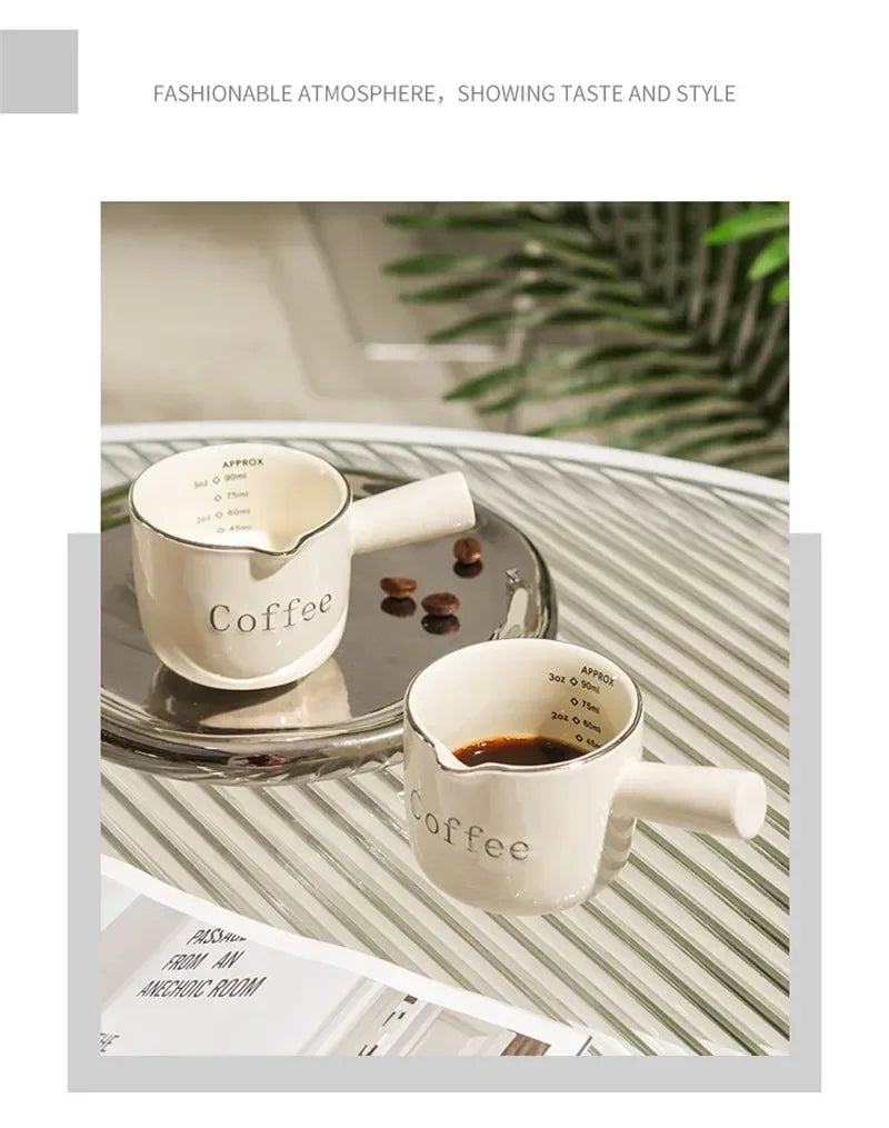 A set of white ceramic espresso coffee cups displayed on a glass tray with green foliage in the background.