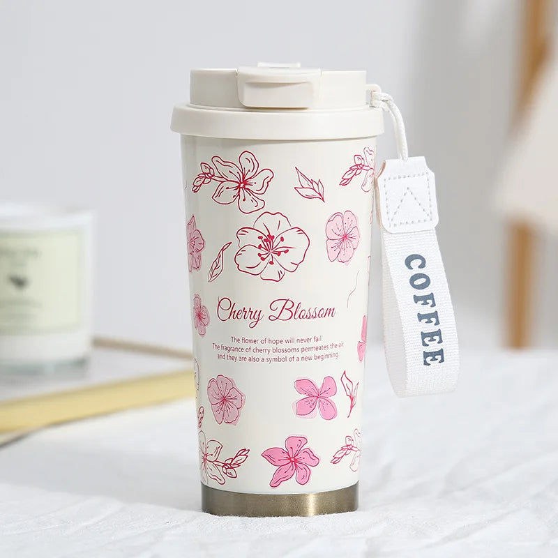 A white insulated stainless steel travel mug with a pink cherry blossom floral design and a white strap.