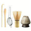A set of natural bamboo tea tools including a ladle, spoon, strainer, and ceramic cup.