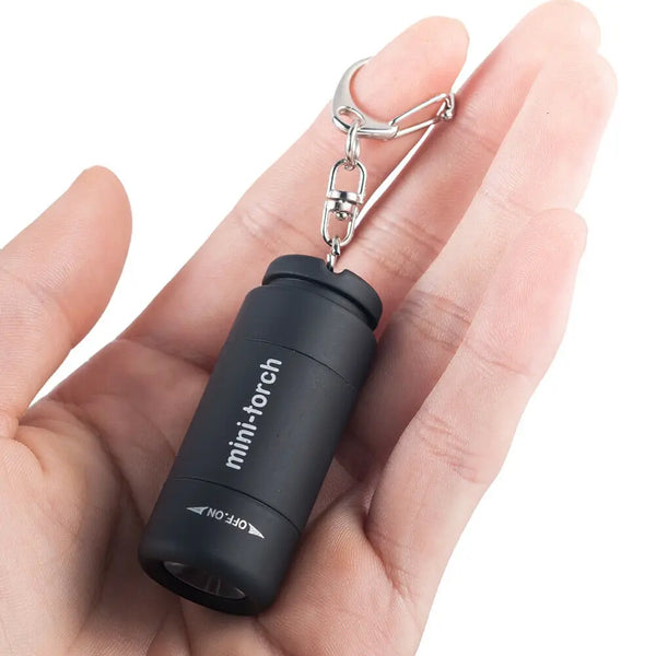 Eine Hand hält eine schwarze Mini-Torch Taschenlampe als Schlüsselanhänger mit silberner Clips.