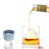 A glass of amber liquid being poured into a glass filled with ice using stackable food-grade molds.