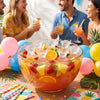 A glass bowl filled with colorful fruit and ice cubes, set on a wooden table with people in the background.