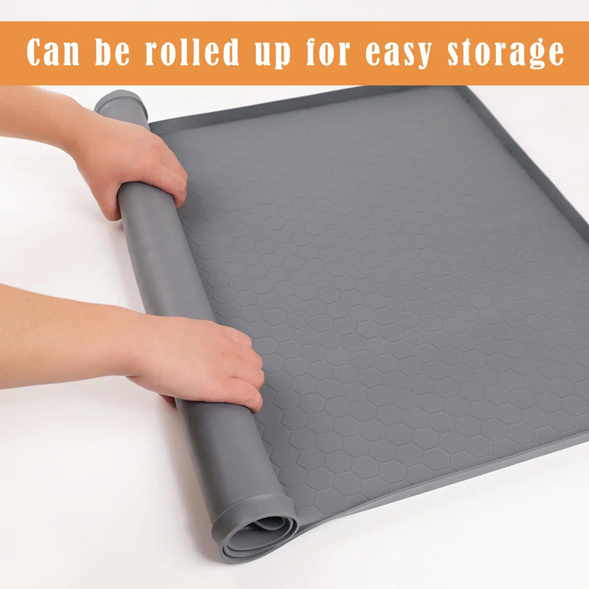 A hand is rolling up a gray silicone under sink drain tray for easy storage.