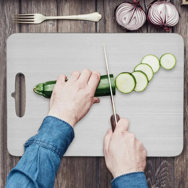 Eine Person schneidet eine Gurke auf einem Edelstahl-Cuttingboard mit einem Messer.