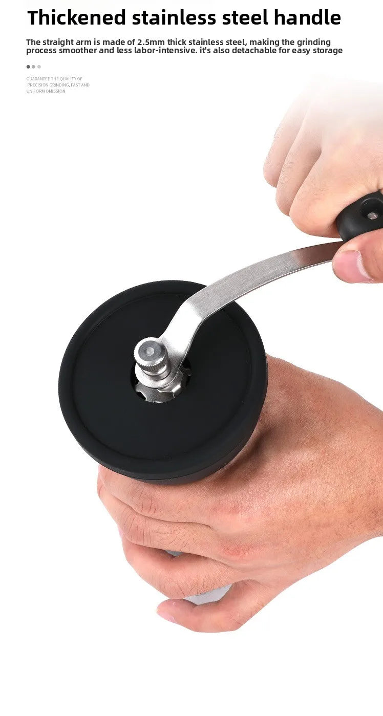 A hand is holding a thickened stainless steel handle of a manual coffee grinder with a black base.