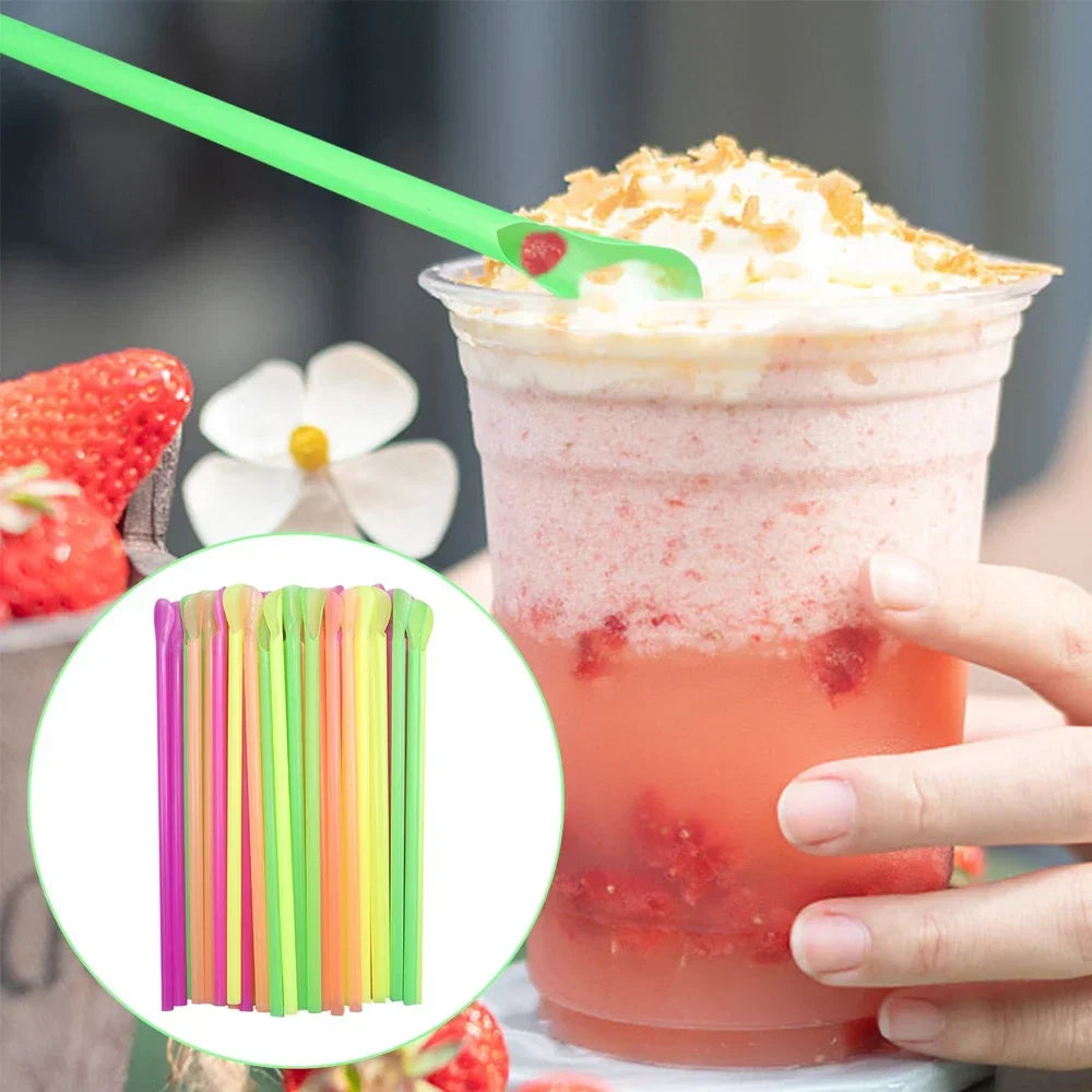 A hand holds a pink beverage with red fruit pieces and is next to a set of colorful reusable plastic stirrers and straws.