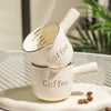 A white ceramic espresso coffee cup set with a measuring guide and a matching handle, resting on a light plate.