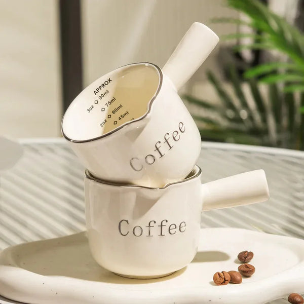 Weißer Keramiktasse für Espresso mit Messleitfaden und passender Henkel auf hellem Teller.