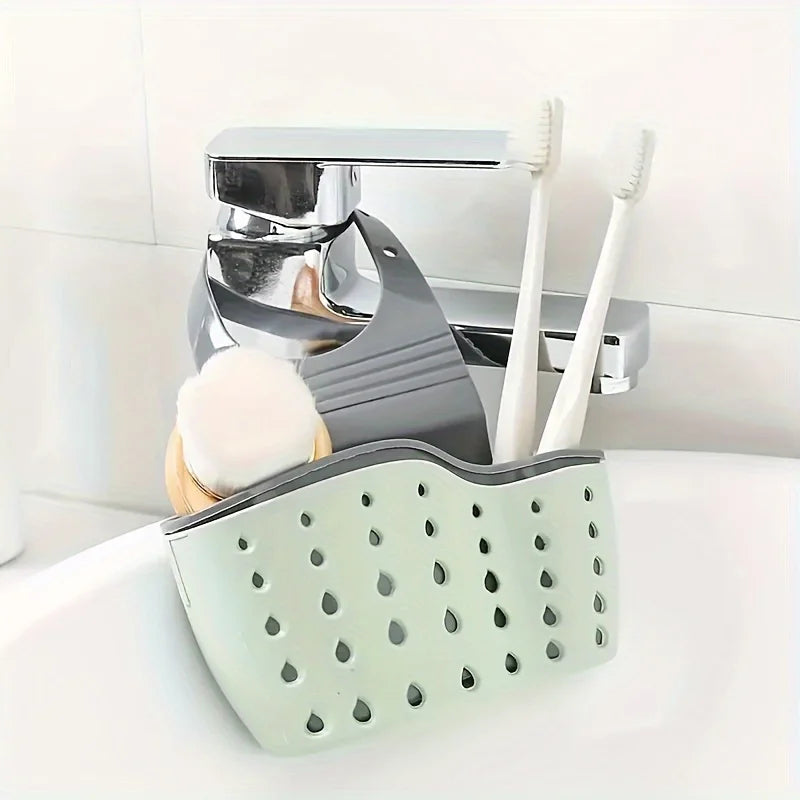 A silver sink drain hanging sponge rack holds a toothbrush and a white sponge.