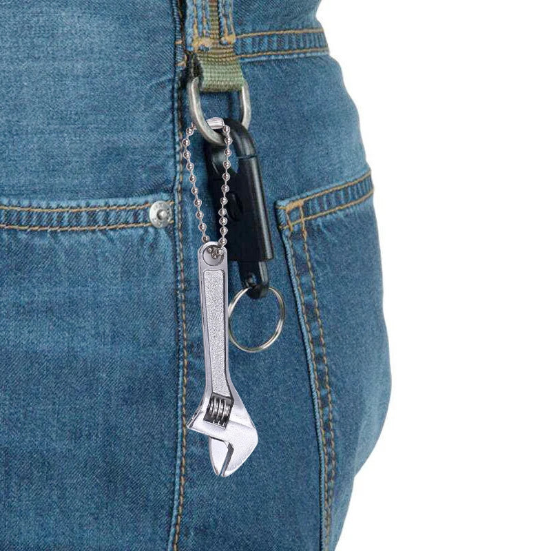 A close-up of a pair of metal tools hanging from a denim pocket, showing a spanner wrench and chain.