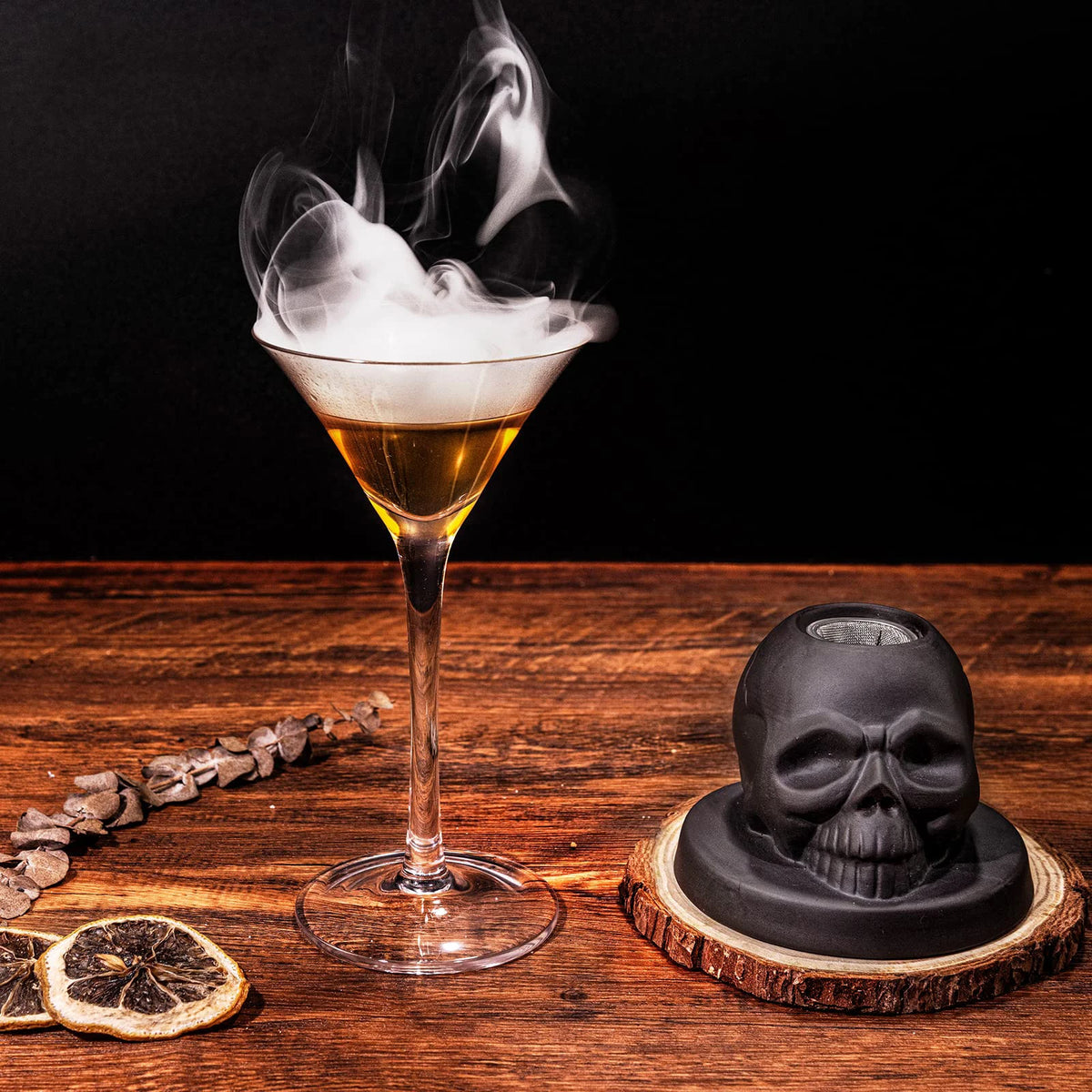 A glass of amber cocktail smoke with a skull-shaped smoker kit and citrus slice on a wooden surface.