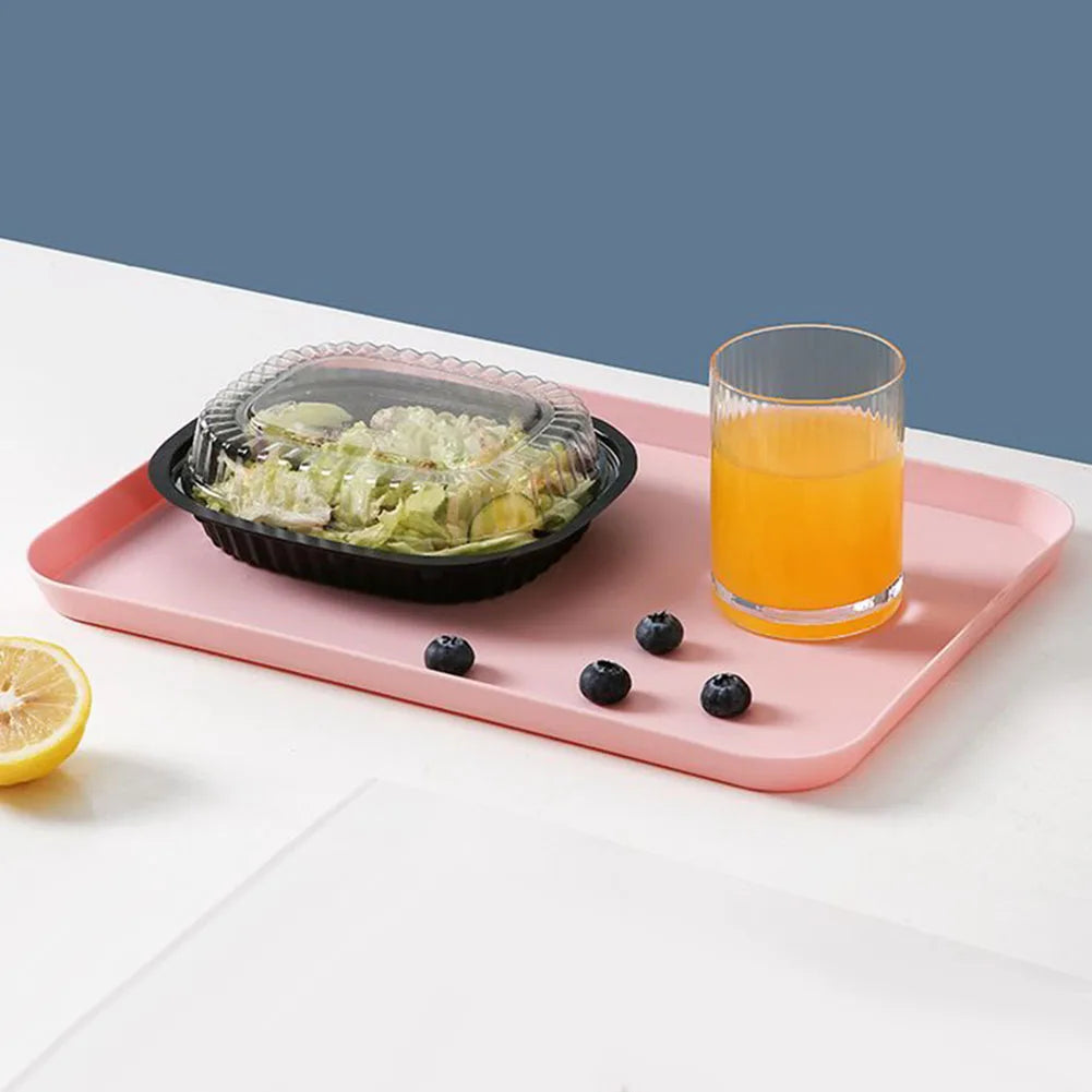 A pink rectangular serving tray holds a glass of orange juice, some blueberries, and a bowl of sliced fruit.