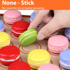 A hand is shown placing or handling pink, red, and green macarons on a silicone baking mat liner.