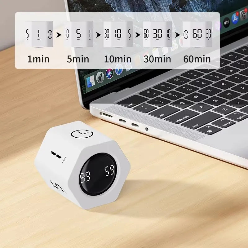 A white productivity cube timer sits on a wooden desk next to an open laptop displaying a countdown timer.