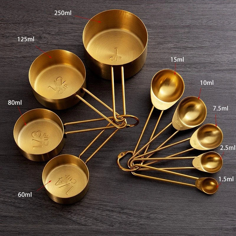 A set of brass measuring cups and spoons with various volumes displayed on a dark wooden surface.
