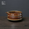 A ceramic matcha whisk pot with an earthy brown glaze sits on a dark wooden surface.