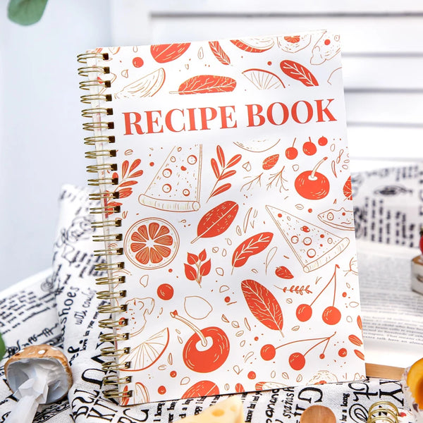 A spiral-bound recipe book with an orange and green floral pattern lies on a white surface.