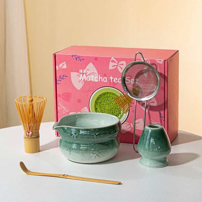 A pink box containing a Japanese matcha tea set with a ceramic bowl, bamboo whisk, and strainer on a white surface.