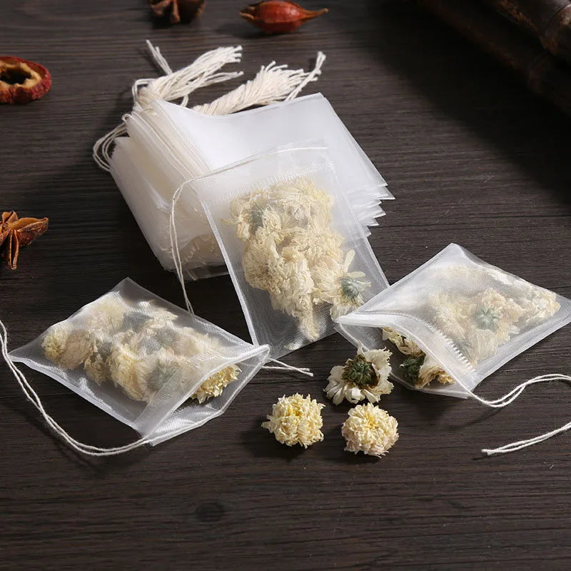 Several clear disposable tea filter bags with drawstrings containing loose tea and spices are displayed on a dark wooden surf