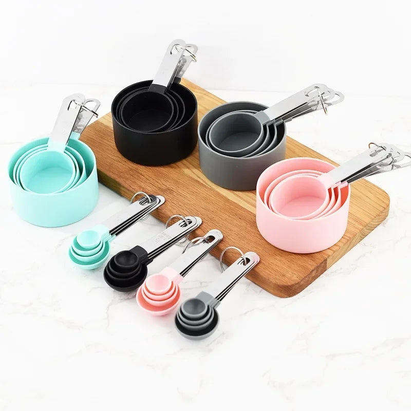 A set of stainless steel measuring cups and spoons in various pastel colors arranged on a wooden board.