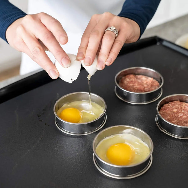 Hands are using a white piping tip to dispense batter into small metal rings for baking.