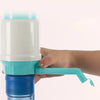 A hand is holding a manual bucket water pump dispenser with a white and teal body and a blue base.
