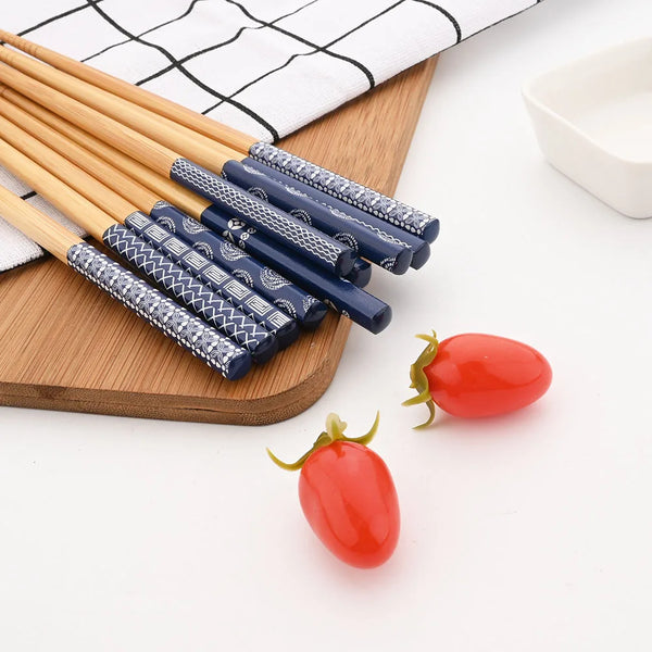 A set of reusable bamboo chopsticks with patterned tips resting on a wooden board next to a red cherry tomato.