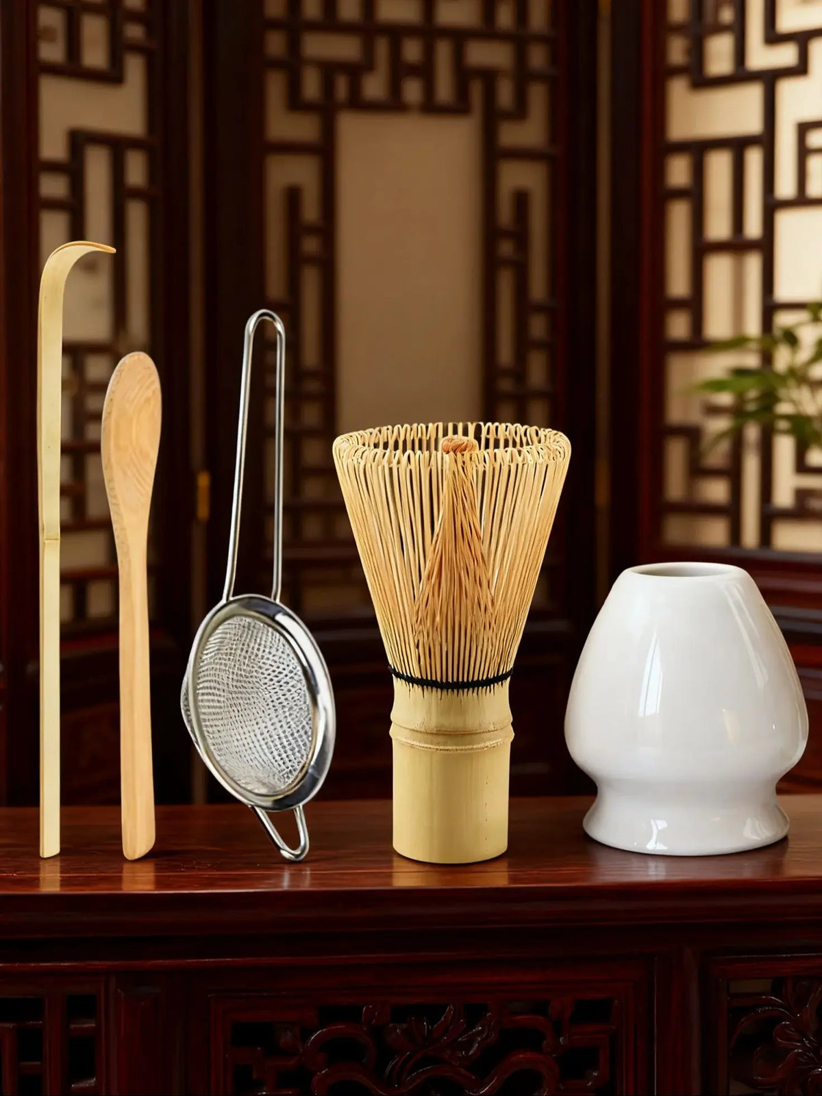 A set of bamboo and metal tools for matcha tea preparation, including a whisk, spatula, and bamboo sieve.