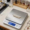 A silver digital kitchen scale with a white pearl decoration is placed on a wooden surface.