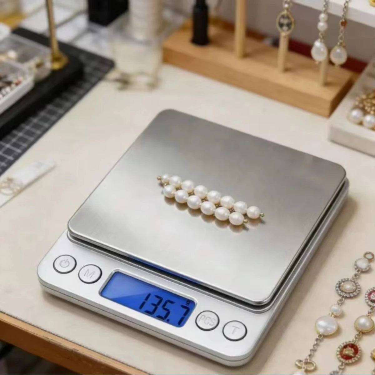 A silver digital kitchen scale with a white pearl decoration is placed on a wooden surface.