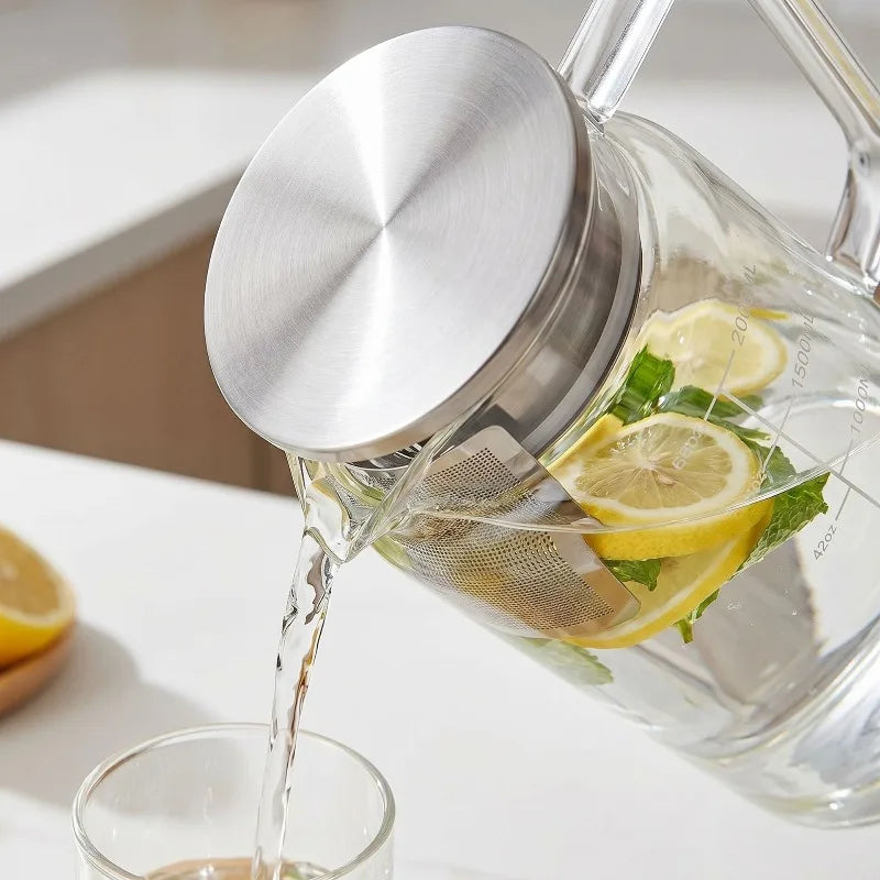 A clear glass water jug is pouring liquid into a glass, with lemon slices and mint leaves visible inside.